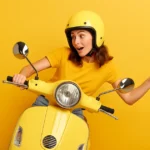 Studentessa sorridente in scooter giallo con casco, simbolo di ottimismo e sicurezza per gli esami 2025 con diritti DSA